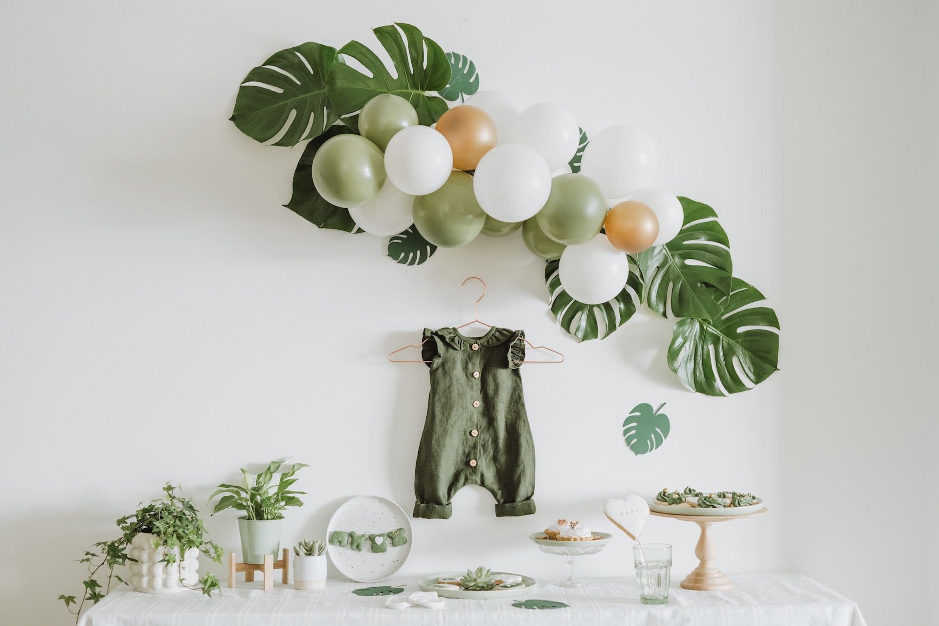 Baby shower decorations on a white tablecloth. Green bab pinafore hangs on the wall above table. 