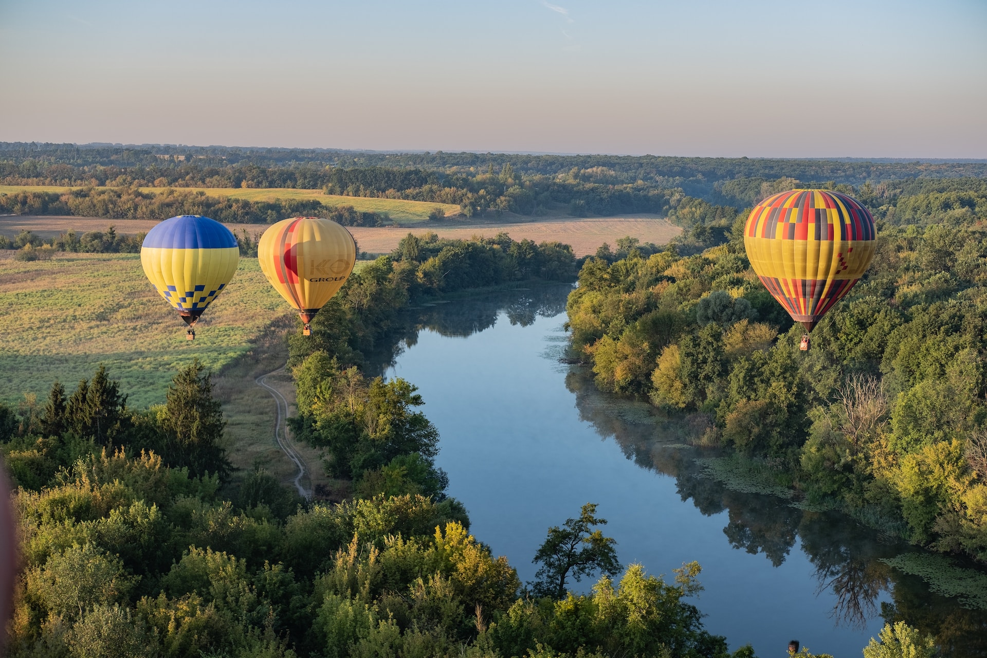 3 hot air balloons over fields and a river.