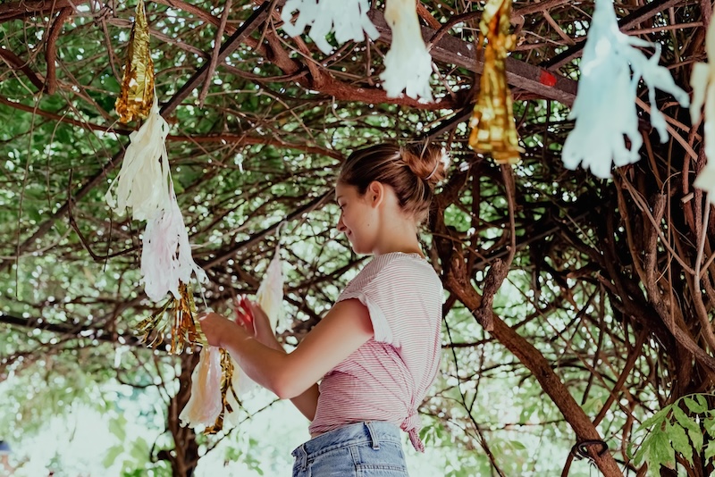 Woman hanging up gold and silver paper streamers in a tree.