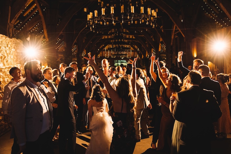 Inside Tithe Barn, wedding party dancing in room lit up by fairy lights and candles overhead.
