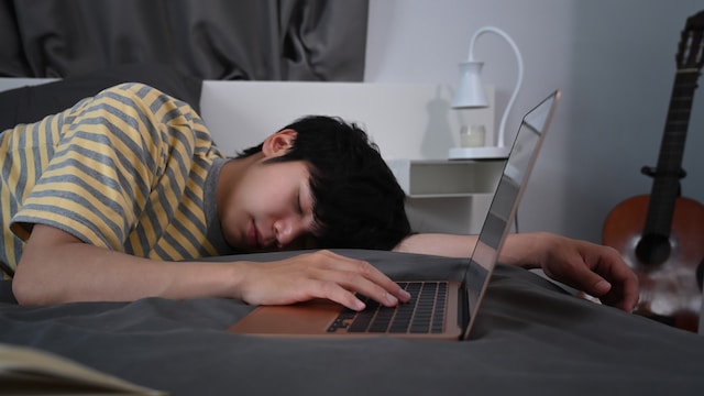 Tired young man sleeping on bed near laptop. 