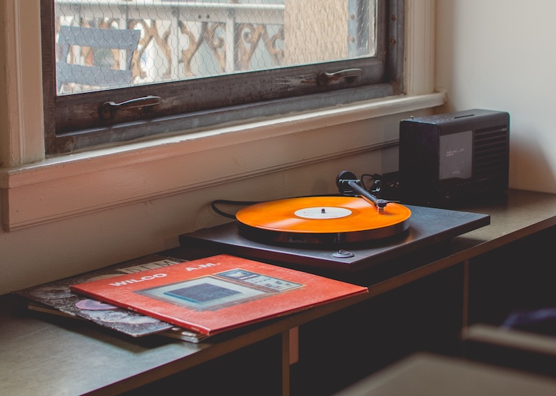 Turntable with orange vinyl playing sits by a window. 