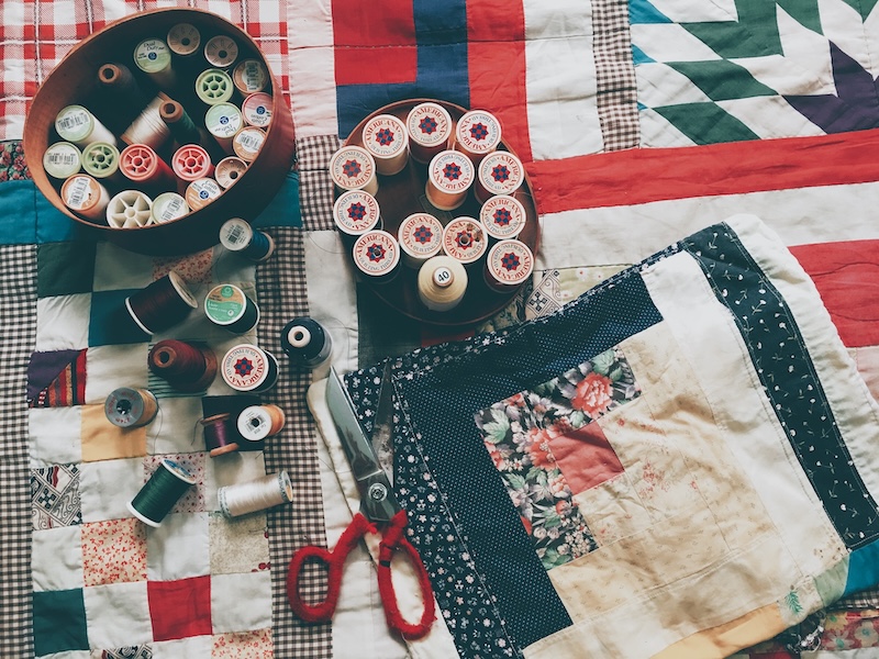 Patchwork quilt being constructed with sewing thread and scissors placed on top.