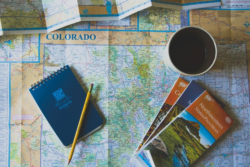 Folded up maps, coffee and a notebook sitting on top of an open map of Colorado.