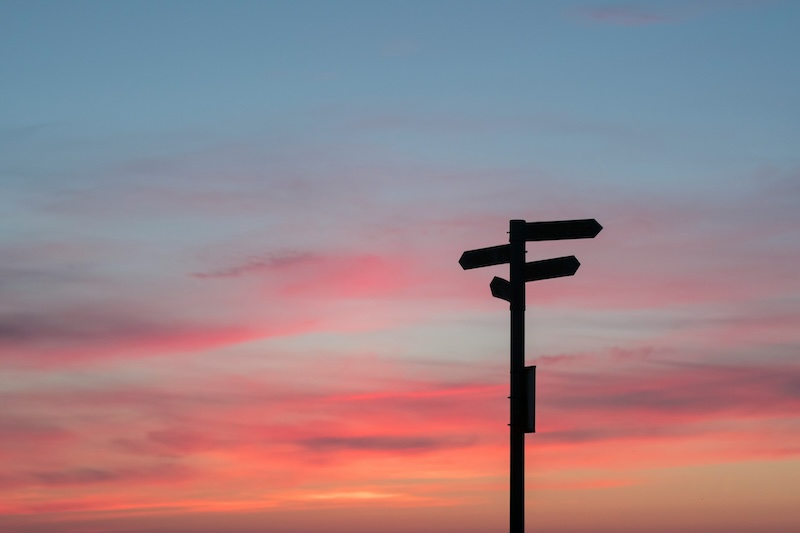 Sunset behind signpost pointing in different directions.