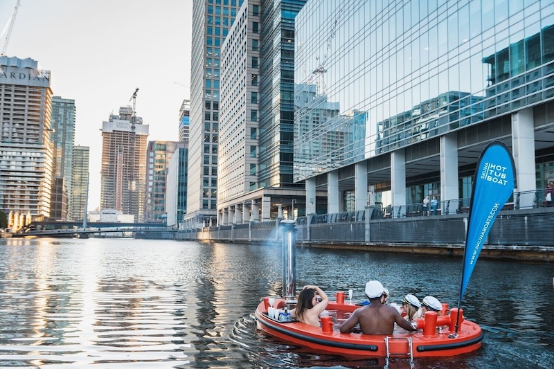 A Skuna hot tub boat in Canary Wharf Canal with a group sat in.