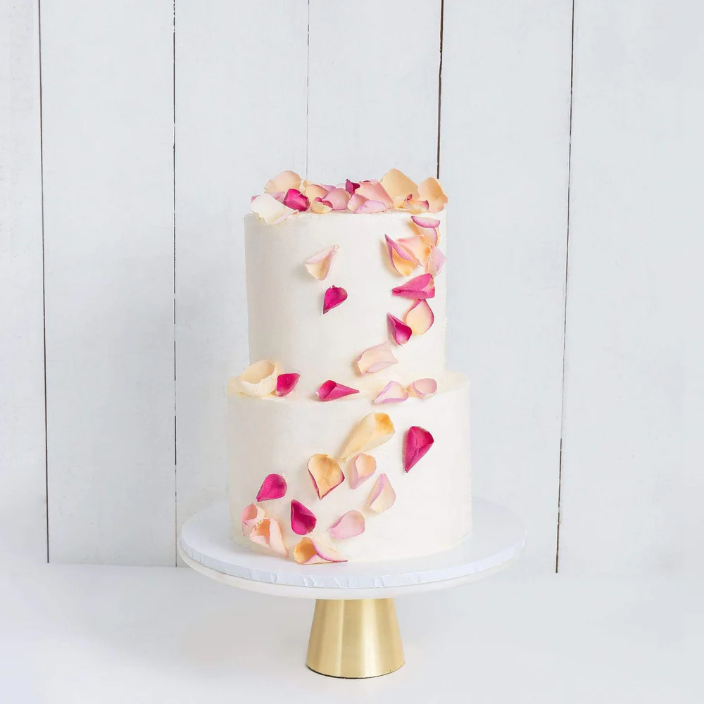 2 tiered white wedding cake decorated with pink and white petals. 