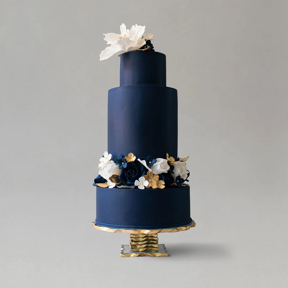 Tall 3 tiered wedding cake with dark navy icing and icing flowers. 