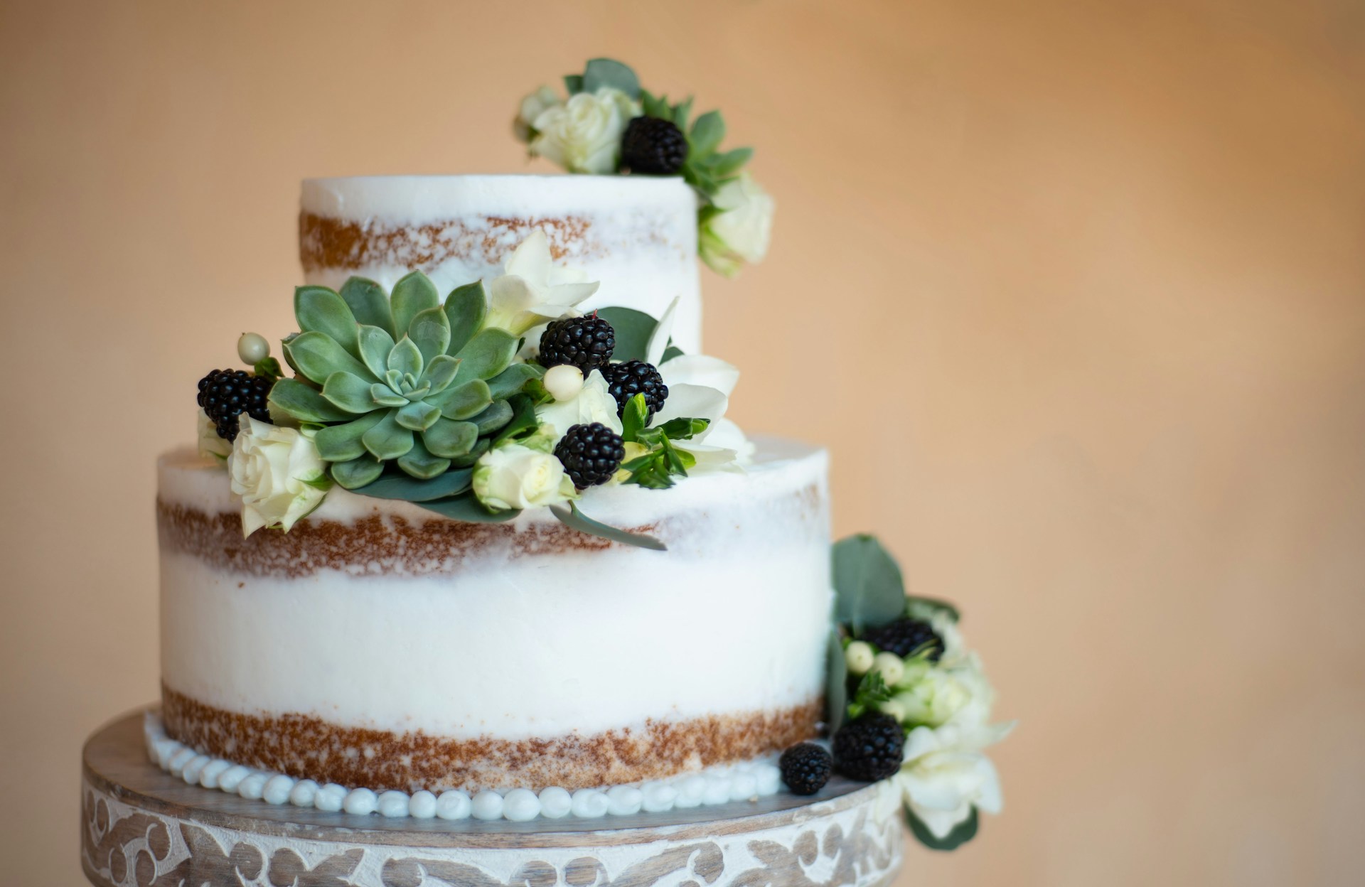 Naked wedding cake decorated with succulents, white roses and blackberries. 