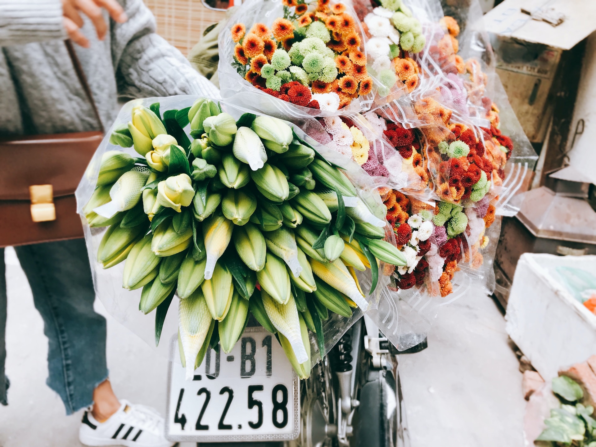 Several bunches flowers strapped to the back of a motorbike. 