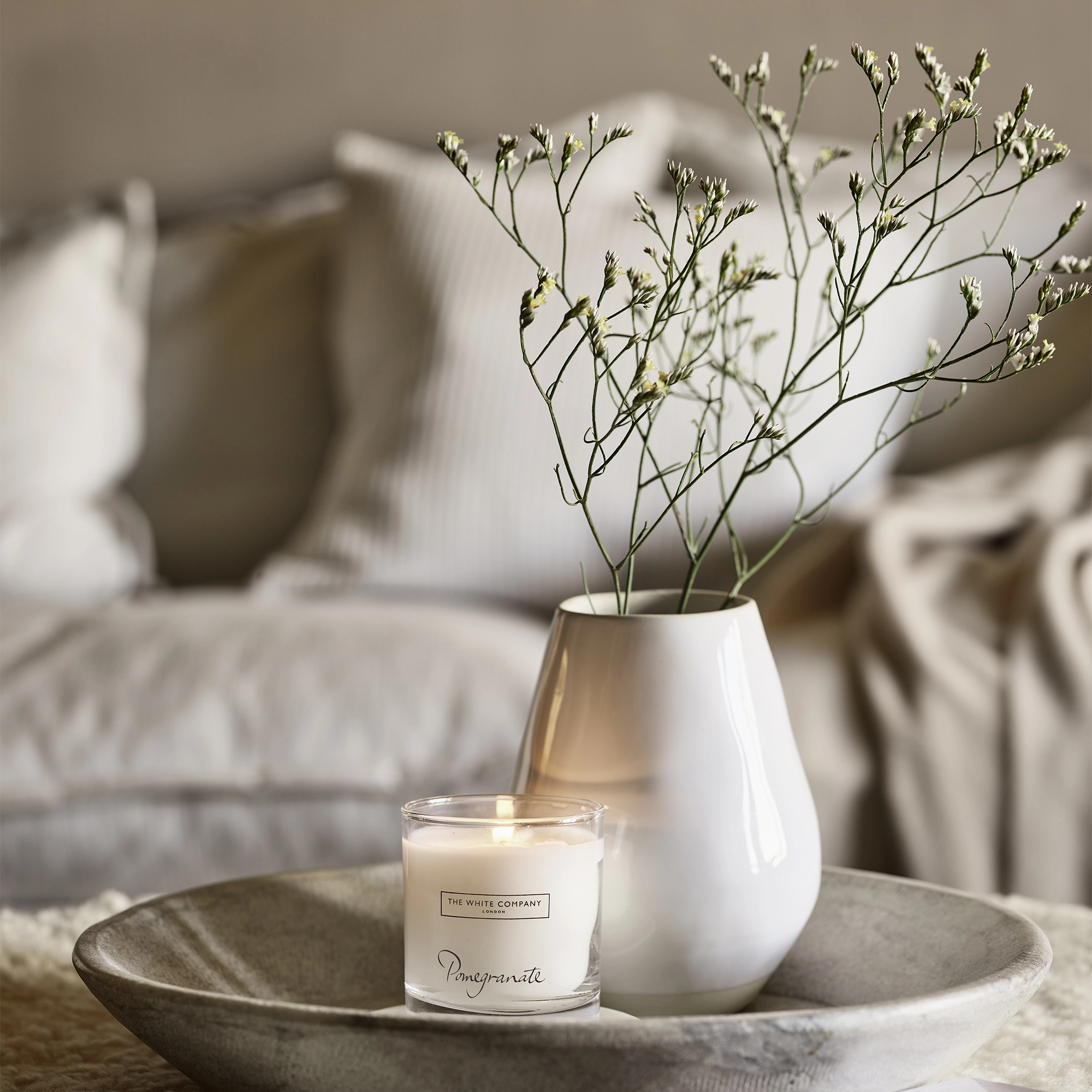 The White Company vase with flowers in and candle stand in grey dish. 